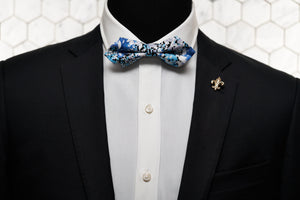 An image of a mannequin modelling a blue diamond pointed bow tie with a golden fleur de lis lapel pin.