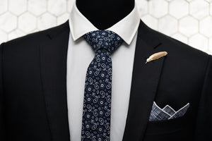 A mannequin is wearing Dear Martian's men accessories, which features our navy paisley tie, the Pratt navy pocket square, and Veder gold feather lapel pin.