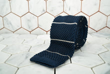 A product image of the Dear Martian midnight navy silk knitted necktie featuring white stripes; the tie is rolled against hexagon tile background.