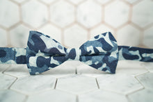 An image of the Shipyard, a denim navy camo patterned bow tie. The Dear Martian bowtie is sitting against a hexagon tiled background.