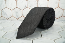 A black denim necktie made by Dear Martian, Brooklyn is shown rolled up and displayed against a hexagonal background.