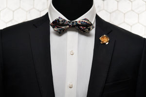 An image of a mannequin wearing the Enchanted, handmade rose gold flower lapel pin and paisley novelty bowtie.